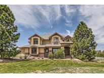 Stunning two-story home with a well-manicured lawn and mature trees under a partly cloudy sky at 6411 Sand Rose Ct, Castle Rock, CO 80108