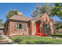 Charming brick home featuring a bright red front door and awning, complemented by lush green lawn and classic shutters at 1235 Dahlia St, Denver, CO 80220