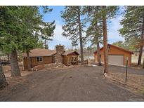 Charming log cabin-style home with a stone chimney and detached garage surrounded by mature trees at 27888 Richmond Hill Rd, Conifer, CO 80433