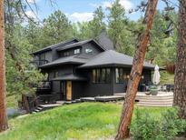 Stunning exterior of a modern two-story home with a deck, lush lawn, and mature trees, nestled in a tranquil setting at 28833 Western Dr, Evergreen, CO 80439