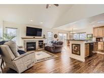 Open-concept living room with a fireplace, television, and hardwood floors connecting to the kitchen and dining area at 6187 Terry Way, Arvada, CO 80403
