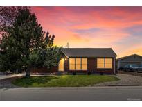 Charming brick home with a well-maintained lawn and a large tree, illuminated by a colorful sunset sky at 160 Northglenn Dr, Northglenn, CO 80233