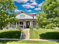 Charming two-story home with a lush lawn, covered porch, and mature trees at 395 Longspur Dr, Brighton, CO 80601
