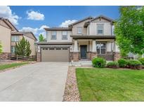 Charming two-story home featuring a manicured lawn and a welcoming front porch with stone accents at 676 Fossil Bed Cir, Erie, CO 80516