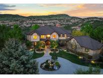 Stunning exterior elevation of grand home, with manicured front yard and mountain views at sunset at 9650 S Cougar Rd, Littleton, CO 80127