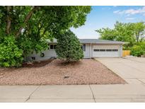 Single-story home with well-manicured front yard, gray paint, mature trees, and two car garage at 8231 E Lehigh Dr, Denver, CO 80237