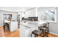 Modern kitchen with white cabinets, marble countertops, stainless steel appliances, and island seating at 13812 W 66Th Dr, Arvada, CO 80004