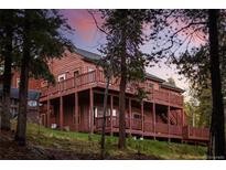 Stunning multi-level home with wood siding and multiple decks, surrounded by lush trees and vibrant sunset colors at 11163 Conifer Mountain Rd, Conifer, CO 80433