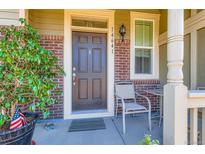 Inviting front entry with brick accents, a cozy chair, and a charming, well-lit porch area at 14641 E Poundstone Dr, Aurora, CO 80015
