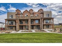 Modern townhome exterior with stone accents, balconies, and lush green lawn under a partly cloudy, bright blue sky at 9629 Browns Peak Cir, Littleton, CO 80125