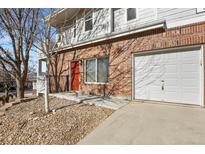 A brick townhouse boasts an attached garage and a vibrant red door adding a pop of color at 5537 Lewis Ct # 101, Arvada, CO 80002