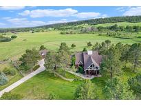 Aerial view of a well-maintained home with mature trees, a long driveway, and surrounded by green fields and forests at 497 Grey Squirrel Way, Franktown, CO 80116