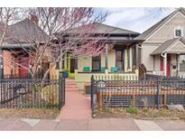 Charming home featuring a covered front porch and decorative wrought iron fence with colorful trees and landscaping at 3313 Curtis St, Denver, CO 80205
