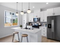 Bright kitchen features white cabinetry, stainless steel appliances, and an island with pendant lighting and barstool seating at 4020 Upham St, Wheat Ridge, CO 80033