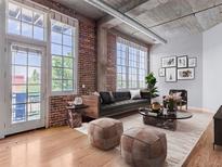 Bright living room with exposed brick, hardwood floors, and large windows overlooking a balcony at 1301 Wazee St # 2D, Denver, CO 80204