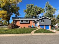 Charming two-story brick home with solar panels, vibrant blue garage doors, and well-manicured lawn at 6107 Xenon St, Arvada, CO 80004