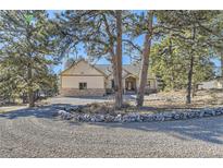 Charming tan home featuring rock accents and a circular gravel driveway with mature trees on a sunny day at 8390 E Summit Rd, Parker, CO 80138