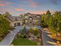 Stately stucco home with stone accents, mature trees, driveway, and landscaping including pond and water feature at 5886 Amber Ridge Dr, Castle Pines, CO 80108