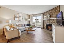 Bright living room with stone fireplace, comfortable seating, and sliding glass doors leading to a balcony at 8225 Fairmount Dr # 106, Denver, CO 80247