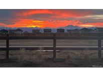 Scenic view of a colorful sunset sky over the neighborhood homes, framed by a rustic wooden fence and distant mountains at 12863 Crane River Dr, Firestone, CO 80504