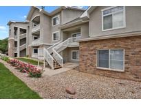 Condo exterior with white staircases, gray facade, brick accents, and landscaped with rocks and flower bushes at 1801 S Dunkirk St # 108, Aurora, CO 80017
