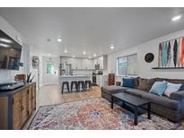 Open-concept living room and kitchen area with gray sofa, modern appliances, island with seating, and colorful rug at 1143 Hummingbird Cir, Longmont, CO 80501