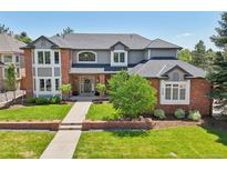 Inviting two-story home featuring a brick and gray exterior, manicured lawn and mature landscaping at 5528 S Jasper Way, Centennial, CO 80015