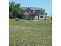 Charming two-story home with a large deck and attached garage is surrounded by an open, grassy lawn at 15300 Cavanaugh Rd, Keenesburg, CO 80643