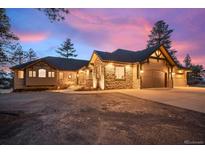 Stunning exterior view of a stone and wood home with a spacious driveway and a colorful sky at dusk at 121 County Road 146, Elizabeth, CO 80107