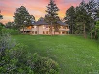 Expansive home featuring large windows, balconies, and a well-manicured lawn, all set against a picturesque sunset at 121 County Road 146, Elizabeth, CO 80107