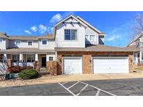 Exterior view of townhome with two-car garage, gray siding, and brick accents at 2550 Winding River Dr # F2, Broomfield, CO 80023