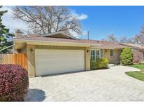 Charming brick home featuring an attached garage and a beautifully paved driveway under a sunny, blue sky at 2243 S Olive St, Denver, CO 80224