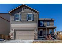 Two-story home features a two-car garage, stone accents, and a covered front porch under a clear blue sky at 579 Jewel St, Brighton, CO 80603