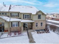 Two-story home featuring stone accents, covered porch, snow-covered roof, and well-maintained landscaping at 5906 S Youngfield Way, Littleton, CO 80127