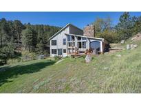 Mountain home with stone chimney, outdoor deck, mature trees, and grassy area at 100 Wildcat Ln, Boulder, CO 80304