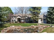 Stunning home exterior with lush lawn, mature trees, and serene pond with rock accents at 7 Mockingbird Ln, Cherry Hills Village, CO 80113