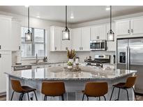 Well-lit kitchen featuring white cabinetry, granite countertops, stainless steel appliances, and a large center island with seating at 8403 Rush Creek Ave, Littleton, CO 80125