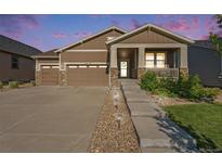 Inviting brown home with a 2-car garage, stone accents, and a welcoming front porch at dusk at 24028 E Caleb Pl, Aurora, CO 80016