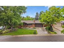 Charming brick ranch-style home with mature trees, lush green lawn, and an attached two-car garage at 7077 Dudley Dr, Arvada, CO 80004
