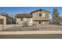 Two-story home with neutral siding, brown roof, gravel yard, and chain-link fence at 7611 Fernando Rd, Denver, CO 80221