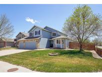 Inviting two-story blue home with stone accents, lush green lawn, and mature trees on a sunny day at 11416 E 114Th Ave, Commerce City, CO 80640