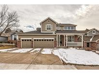 Charming two-story home with a three-car garage and a covered front porch with snow at 240 Corby Pl, Castle Pines, CO 80108