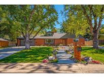 Charming brick home with mature trees, landscaped yard, and concrete steps leading to the front door at 13070 W 15Th Dr, Golden, CO 80401