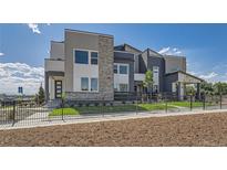 Modern townhome featuring stone accents, neutral siding, landscaped front yard, and metal perimeter fencing at 6880 Bryant Way, Denver, CO 80221