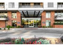 Stunning brick building entrance featuring a modern glass awning and manicured landscaping at 333 S Monroe St # 211, Denver, CO 80209