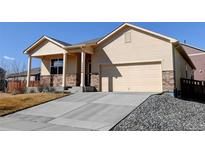 Tan one-story home featuring a two car garage, covered porch, and stone accents at 1799 Jade Ave, Brighton, CO 80603