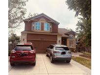 Two-story home with brick accents, attached garage, and driveway with two parked cars at 20410 Kelly Pl, Denver, CO 80249
