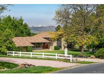 Charming home exterior featuring a white fence, lush lawn, and mountain views in the background at 2117 Stonehenge Cir, Lafayette, CO 80026
