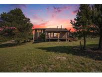 Lovely home with a wooden porch surrounded by trees and an open field at 6880 Kilimanjaro Dr, Evergreen, CO 80439
