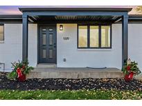 White ranch house with gray door, landscaping, and a covered entryway at 5519 Troy St, Denver, CO 80239